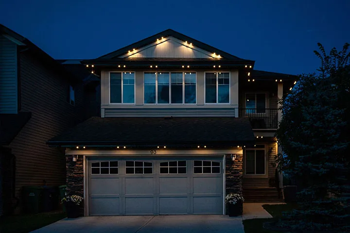 A well-lit house glows warmly against a darkening evening sky