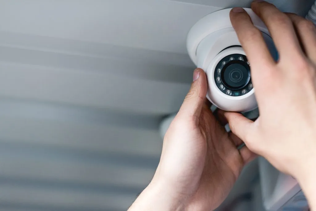 A person installs a surveillance camera on a ceiling