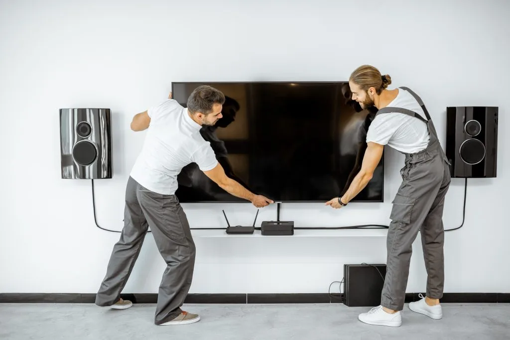 Two men are connecting devices and adjusting a wall-mounted television