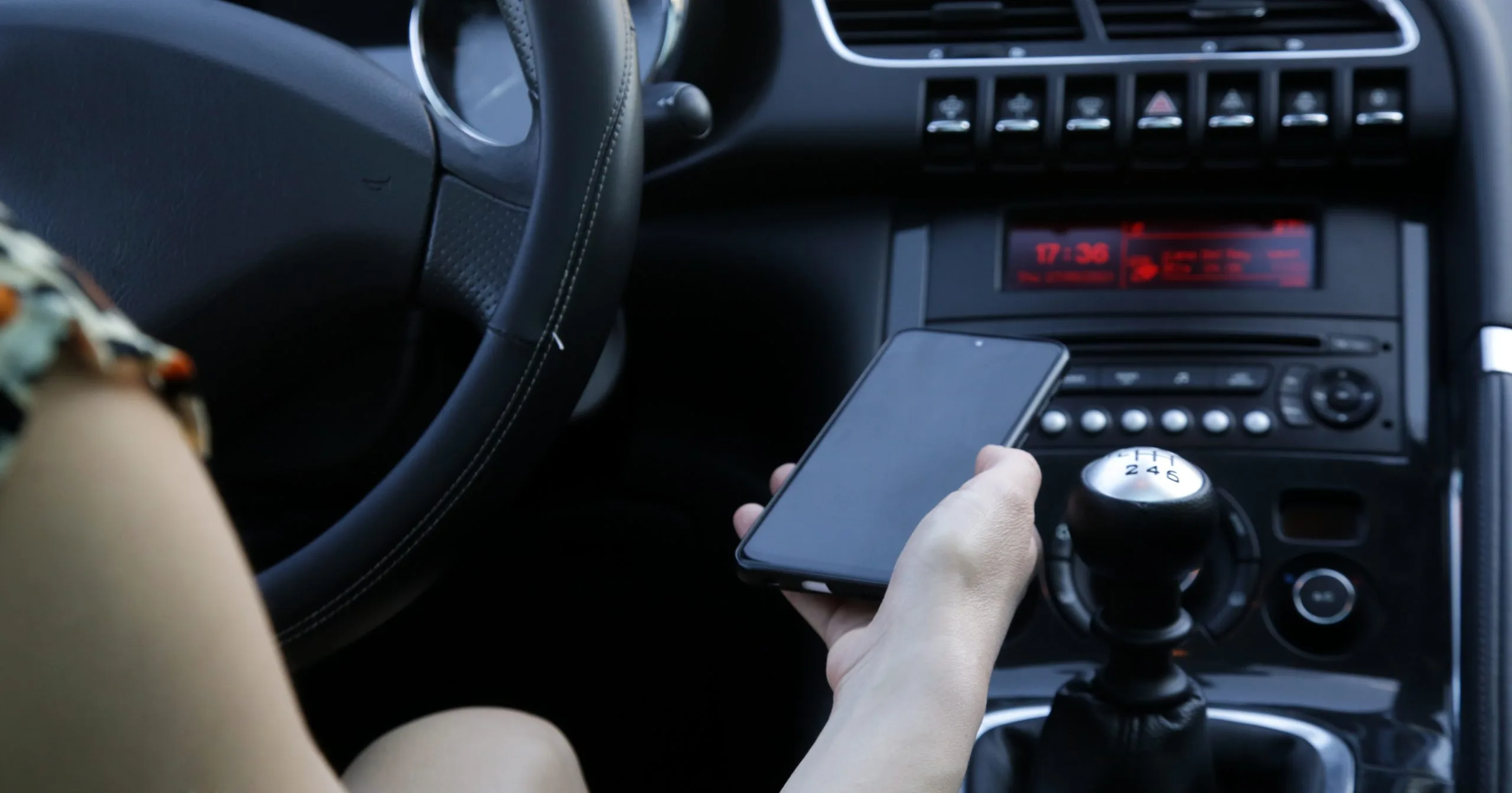 A hand holds a smartphone near the car audio system on the gear shift