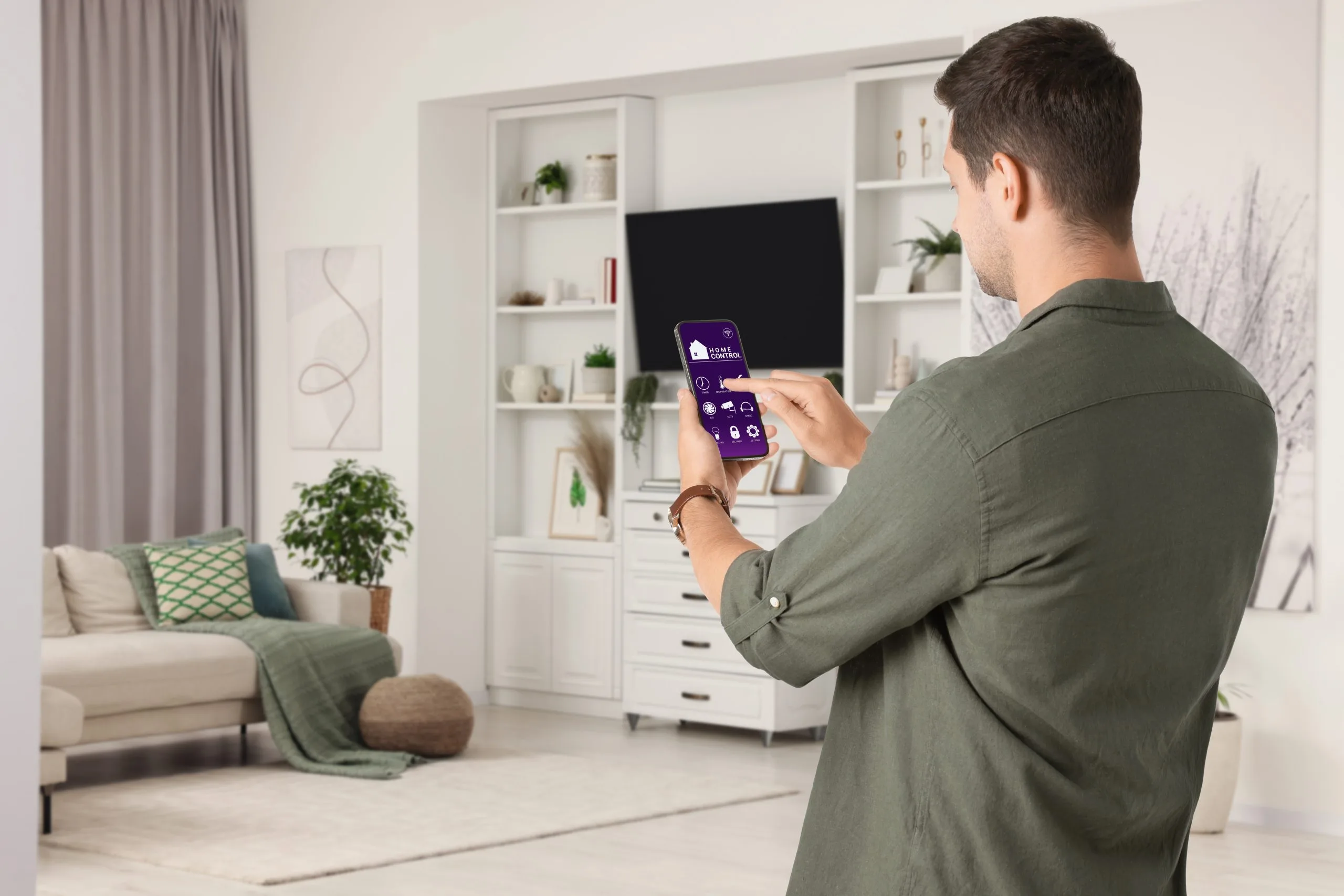 A man controls smart lighting in a modern Winnipeg living room using his smartphone