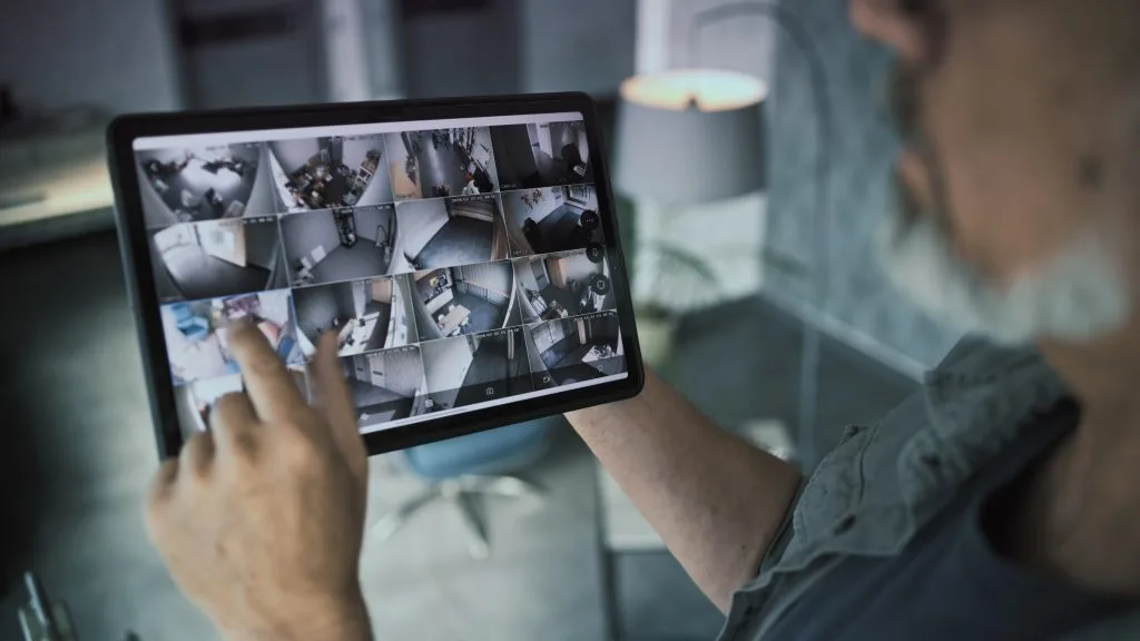Person monitoring video security systems on a tablet with multiple camera feeds