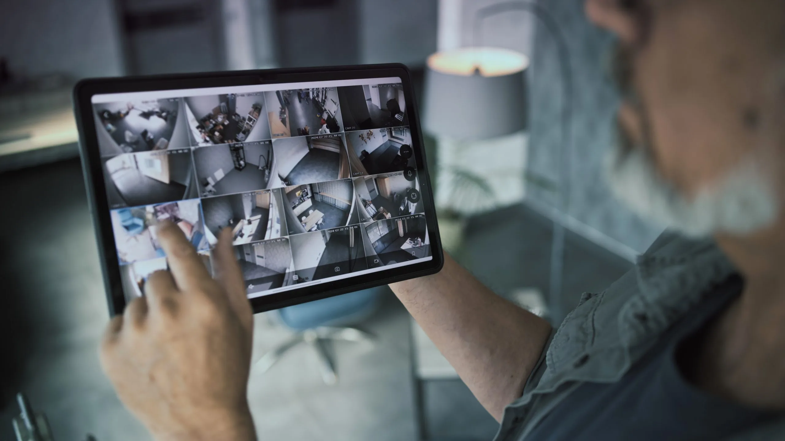 Person monitoring video security systems on a tablet with multiple camera feeds