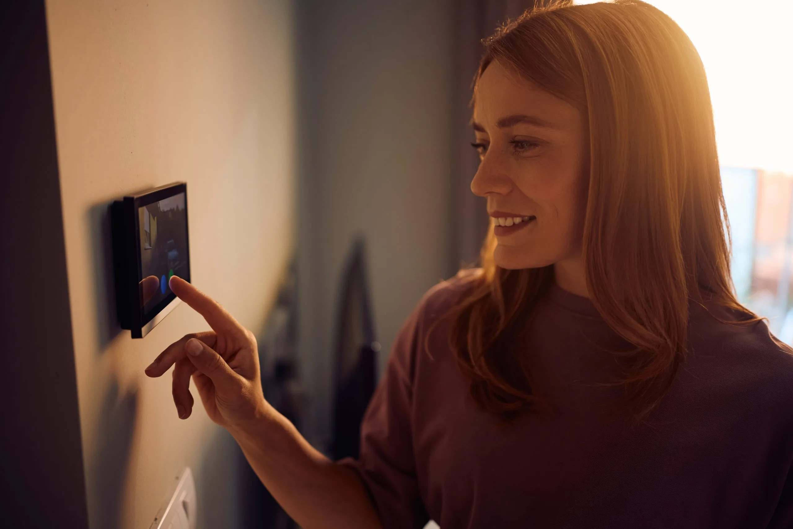 Woman adjusts a smart thermostat, enhancing her home with video security systems