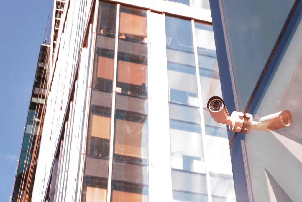 A surveillance camera monitors urban architecture reflecting sunlight