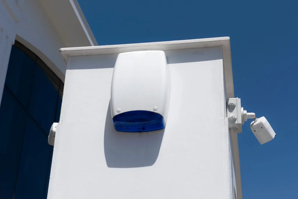 A white security device with a blue light is mounted on a wall