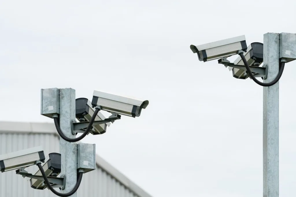 Several surveillance cameras are mounted on posts against a cloudy sky