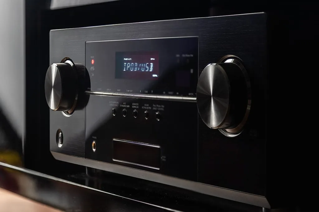 A sleek audio receiver displays digital information with illuminated buttons and knobs