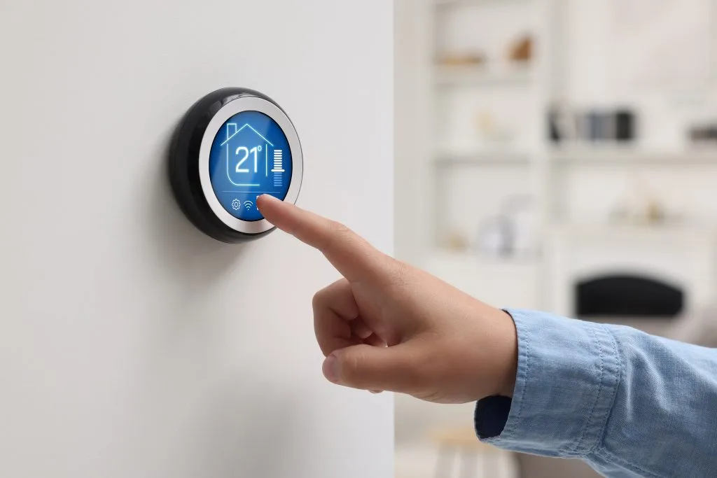 A hand adjusts a digital thermostat displaying the temperature