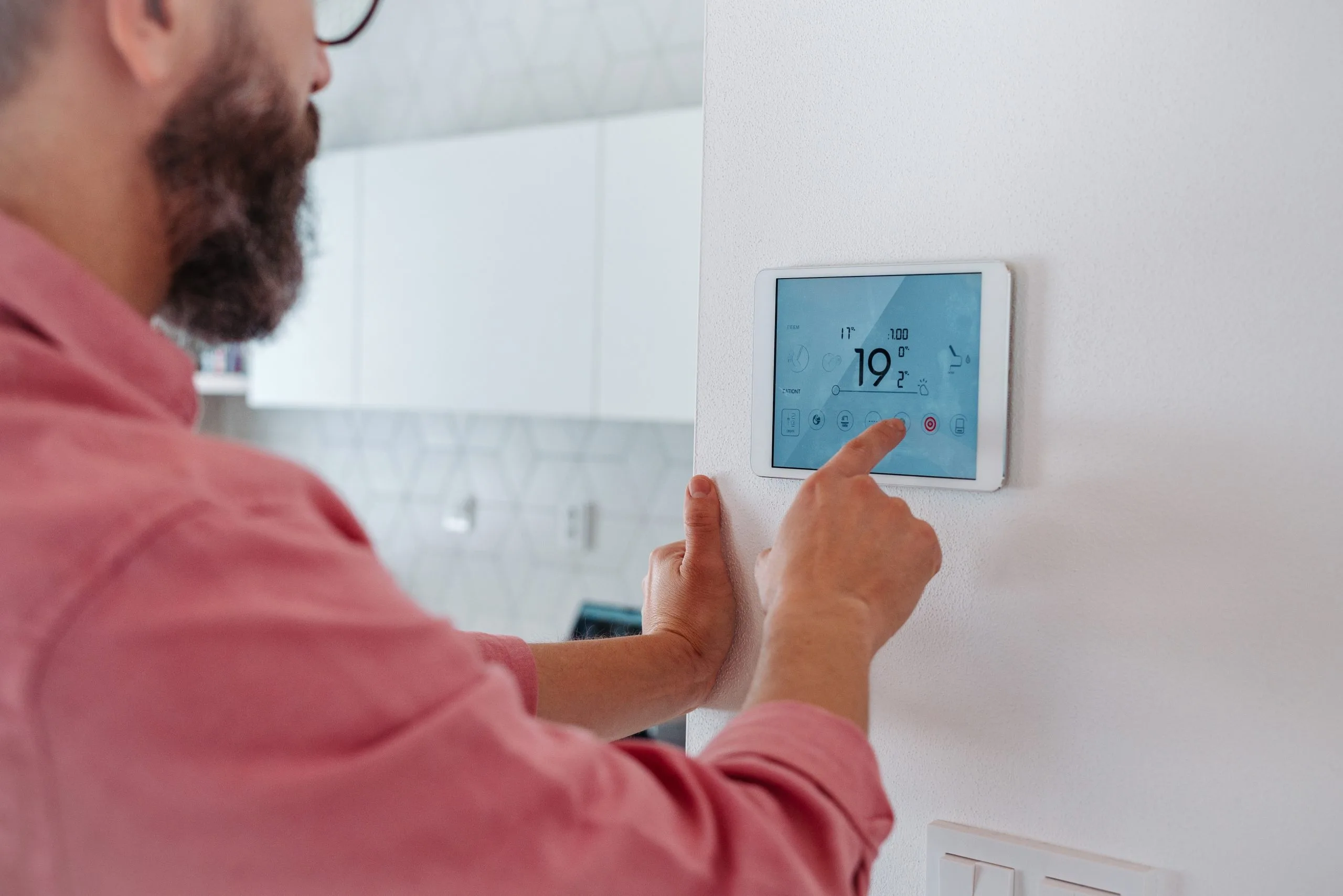 A person adjusts a digital thermostat on a wall