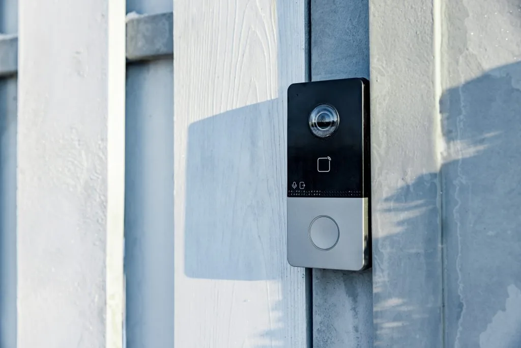 A sleek doorbell camera is mounted on a wooden fence