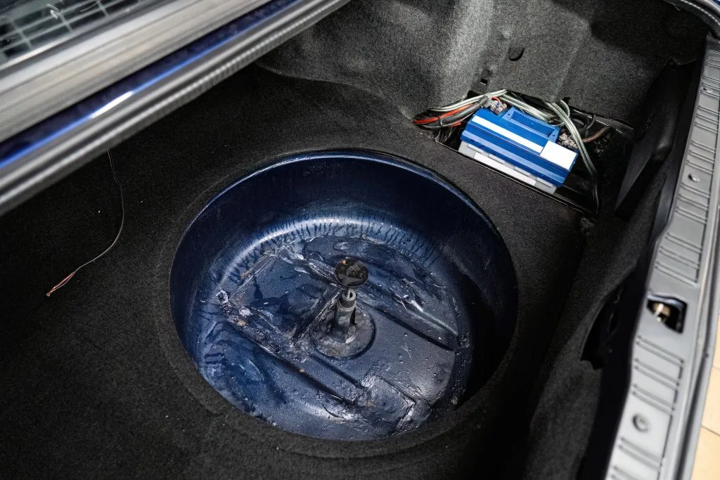 A circular, painted spare tire well sits empty in a trunk, surrounded by dark fabric