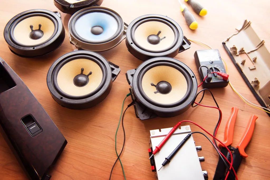 Multiple speakers are arranged on a wooden surface alongside various tools and components