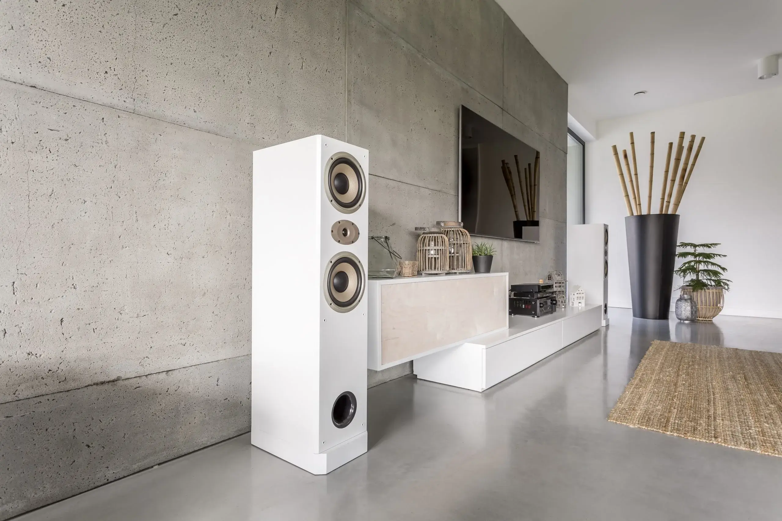 A sleek white speaker stands beside a modern entertainment setup in a minimalist room